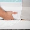 een hand die de wasbare bedonderlegger onder het matras schuift.