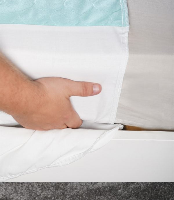 een hand die de wasbare bedonderlegger onder het matras schuift.
